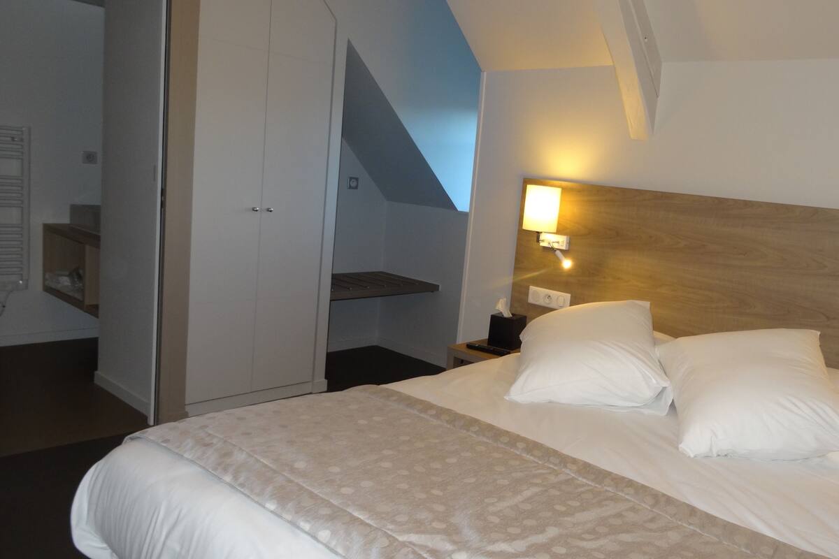 A hotel room with a bed, a nightstand, a wall-mounted lamp, and a wooden headboard.