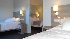 Habitación de hotel con tres camas, cada una con mesita de noche y lámpara de lectura fijada a la pared.
