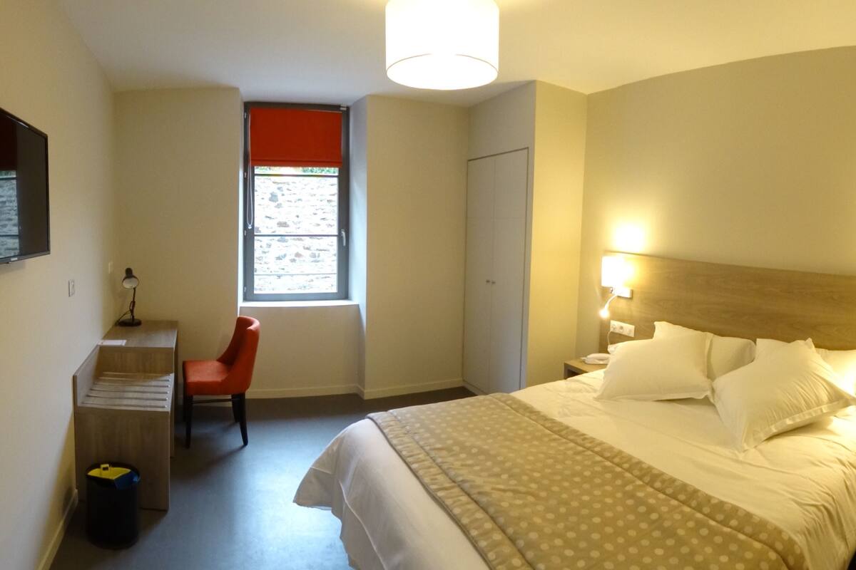 A hotel room with a bed, a desk, a chair, a window, and a wardrobe.