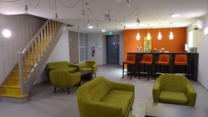 Un vestíbulo con una escalera, sillones verdes, un mostrador de recepción y sillas anaranjadas.