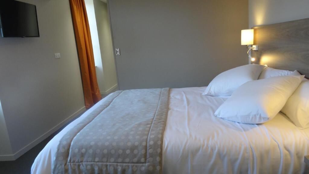 A hotel room with a bed, a TV mounted on the wall, and a lamp on the side of the bed.