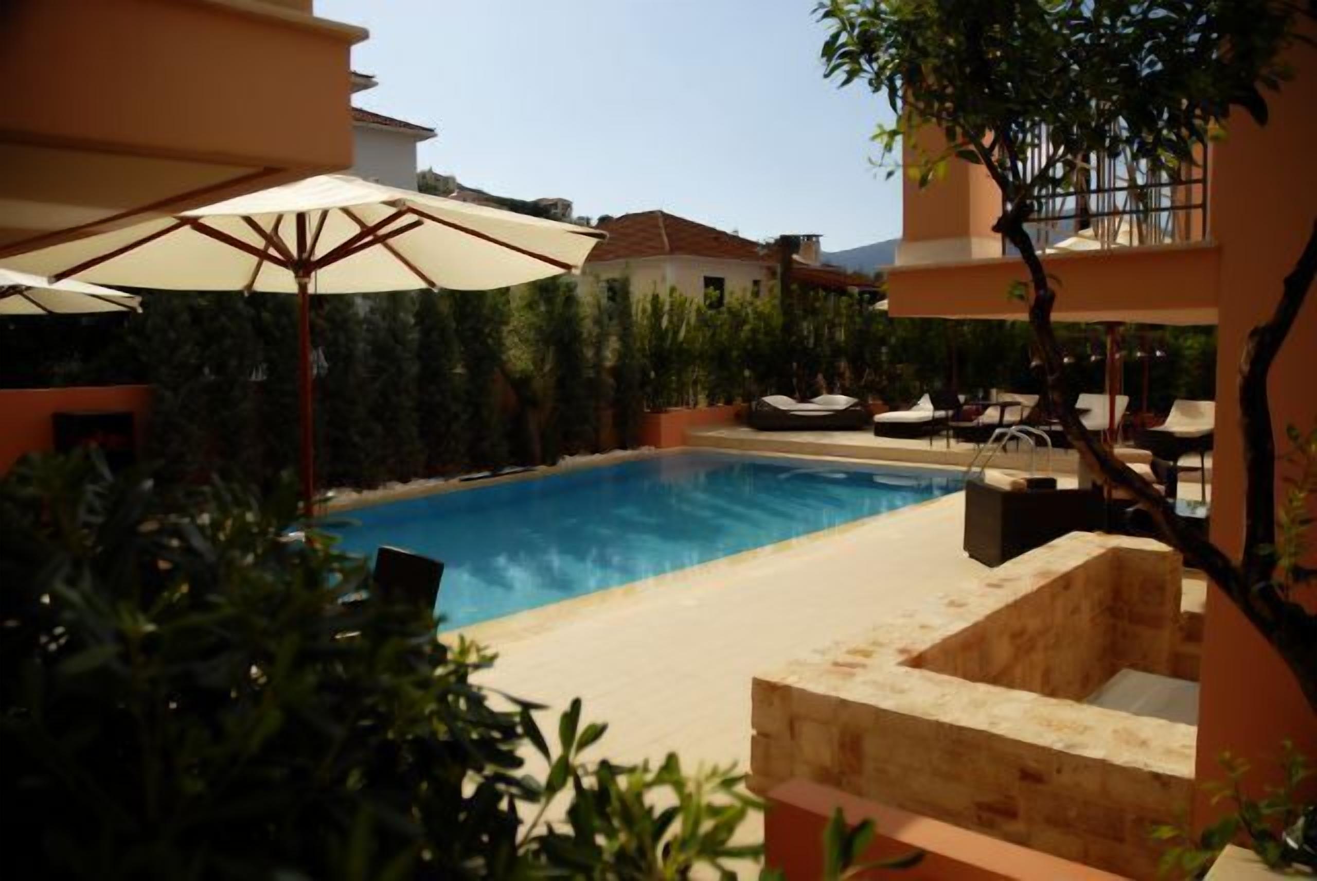 A swimming pool with lounge chairs and umbrellas, surrounded by greenery and buildings.