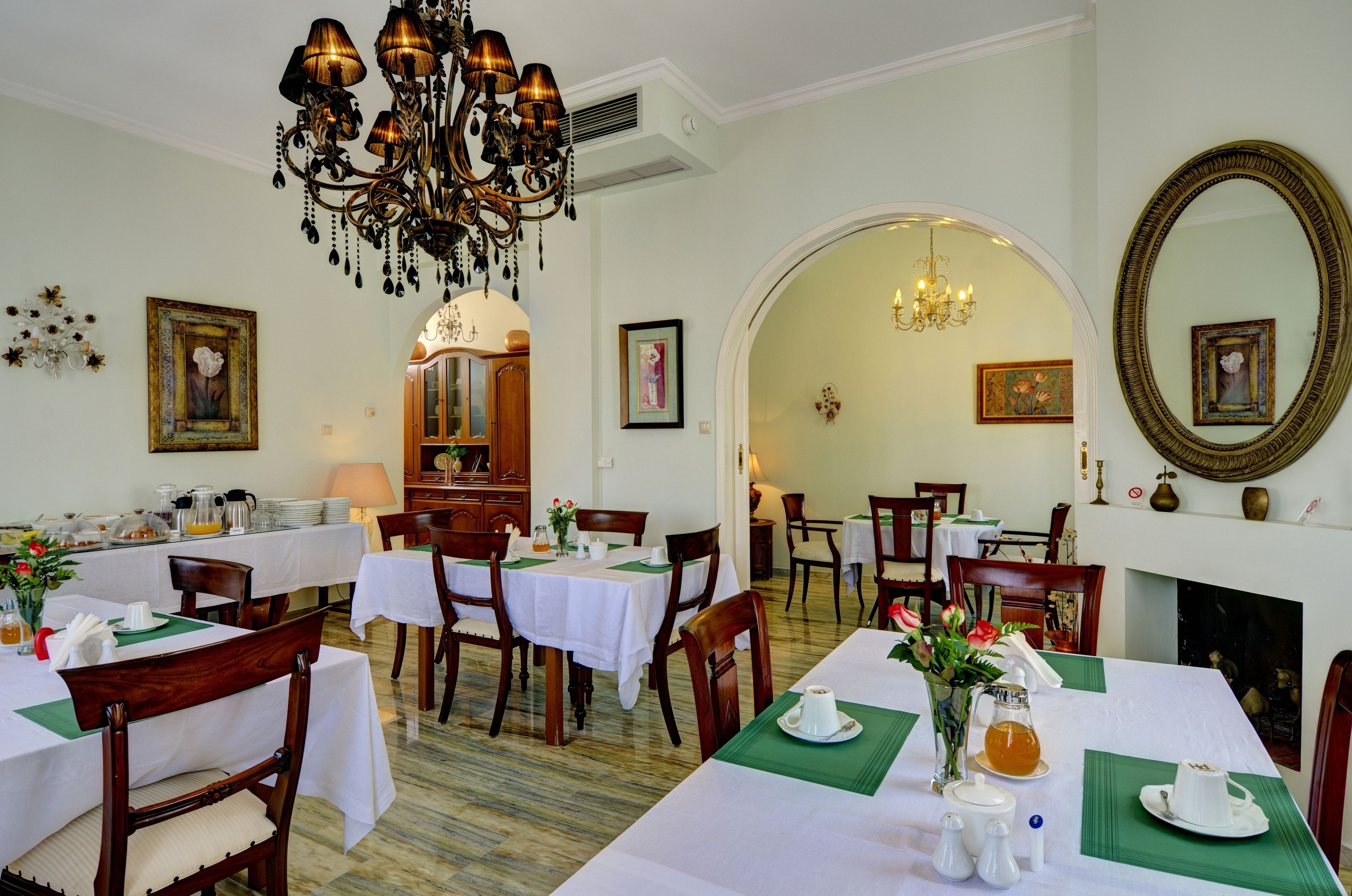 Un espace repas avec des tables préparées pour le petit-déjeuner, agrémenté de nappes blanches, de chaises en bois et de sets de table verts.