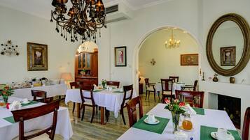 Un espace repas avec des tables préparées pour le petit-déjeuner, agrémenté de nappes blanches, de chaises en bois et de sets de table verts.