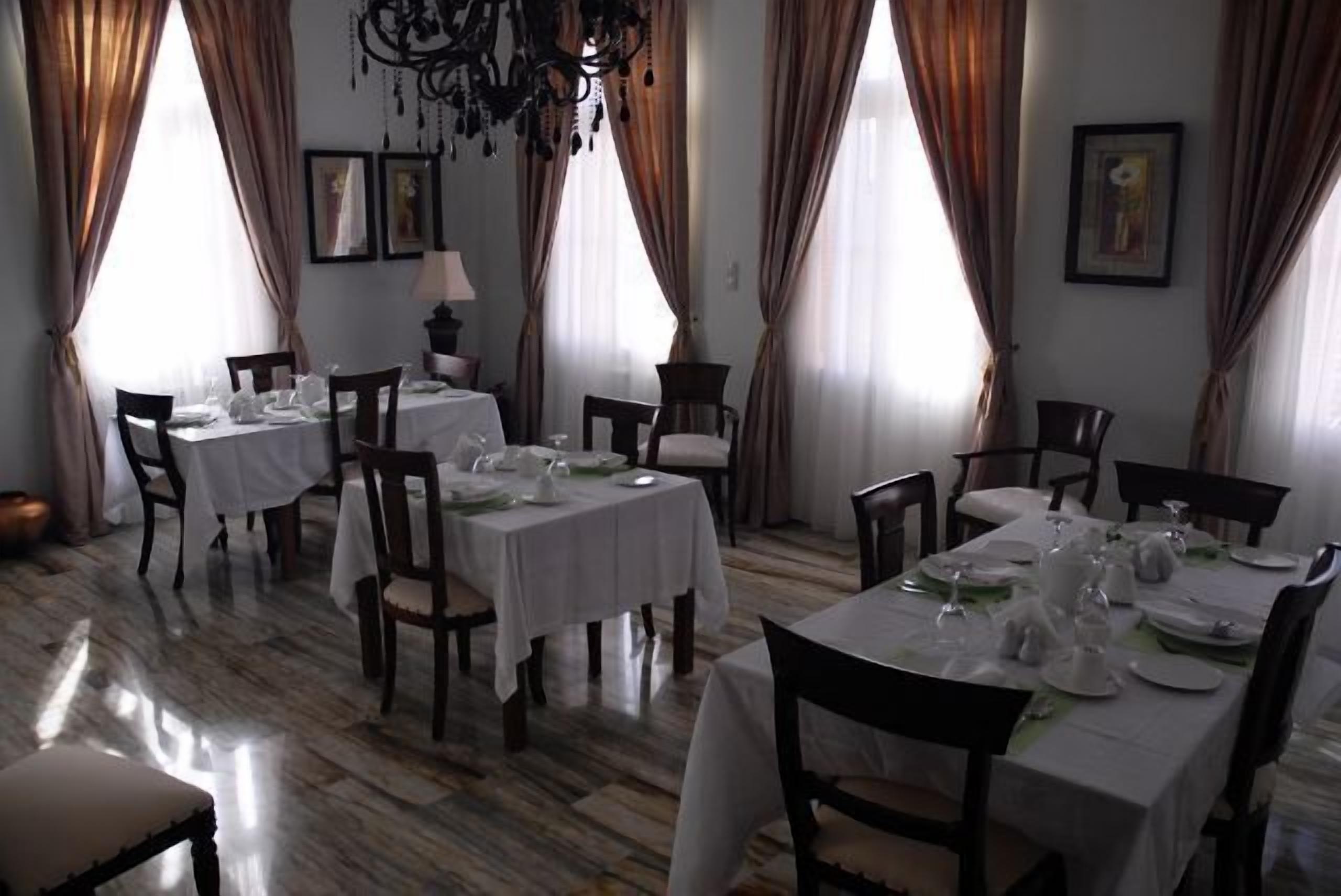 Un comedor con mesas dispuestas para una comida, que cuenta con una araña, cortinas y obras de arte enmarcadas en las paredes.