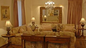 Un salon comprenant un canapé, deux tables d’appoint avec des lampes, un lustre et un grand miroir.