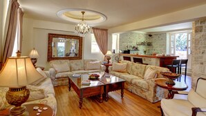 A spacious living room with floral-patterned sofas, a wooden coffee table, and a chandelier. - Korina Gallery Hotel (Ithaki)
