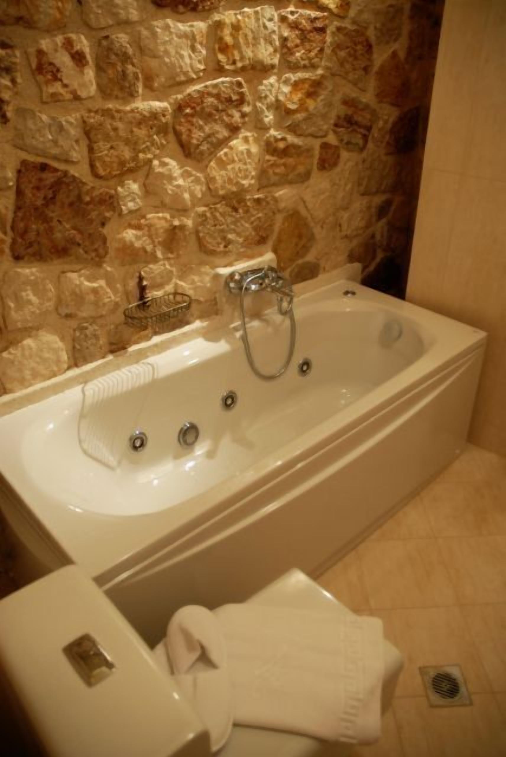 Ein Badezimmer mit Steinwand, einer weißen Badewanne und einem Handtuchhalter.
