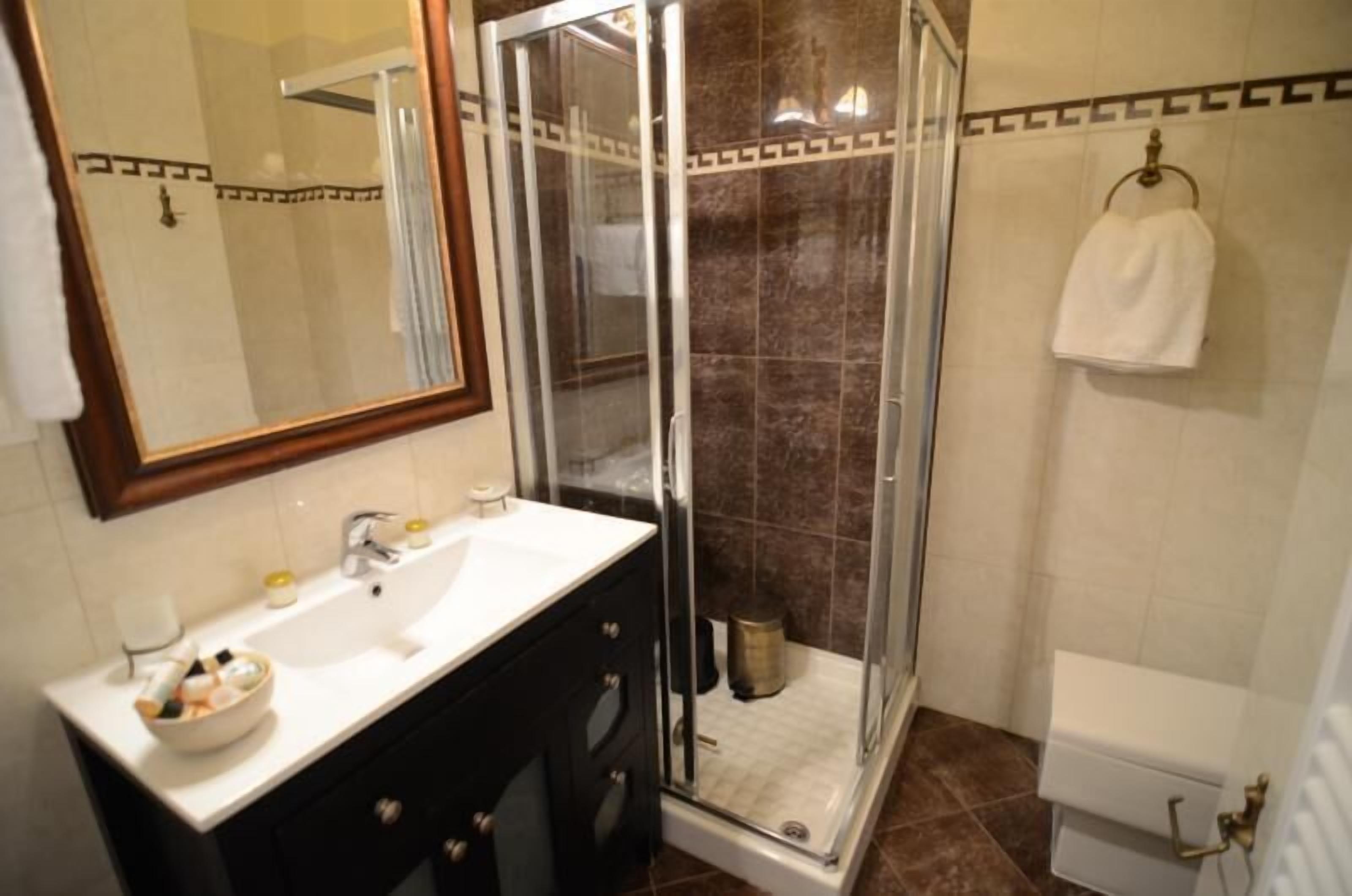 Un baño con ducha de vidrio, un lavamanos blanco con espejo arriba y una toalla colgada en la pared.