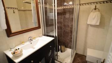 Un baño con ducha de vidrio, un lavamanos blanco con espejo arriba y una toalla colgada en la pared.