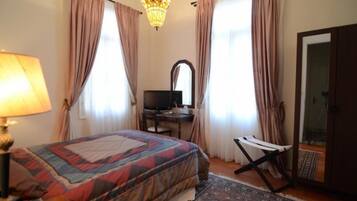 A bedroom with a bed, a desk with a computer, a chair, a mirror, and a chandelier.