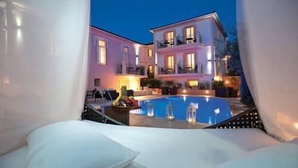 A poolside view of a two-story building with a swimming pool, outdoor seating, and a well-lit balcony. - Korina Gallery Hotel (Ithaki)