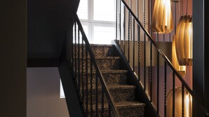 A staircase with a dark railing and granite steps, leading to a landing with a large window. - B&B Zakske 13 (Bruges)
