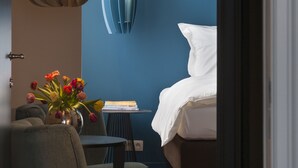 A modern bedroom with a blue accent wall, a round hanging light, a bedside table with a book, and a bed with white linens. - B&B Zakske 13 (Bruges)