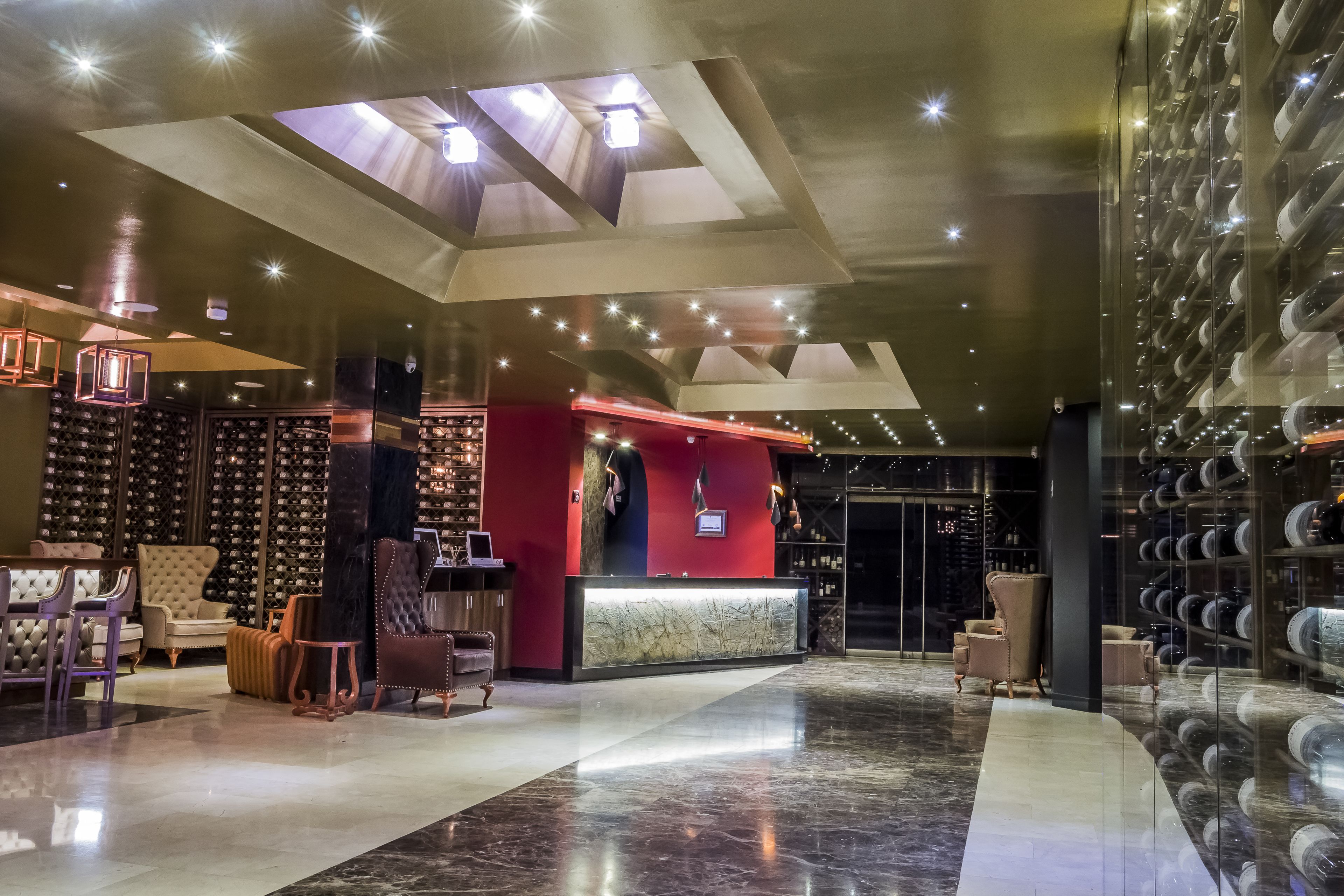 A modern hotel lobby with a reception desk, seating area, and wine racks.