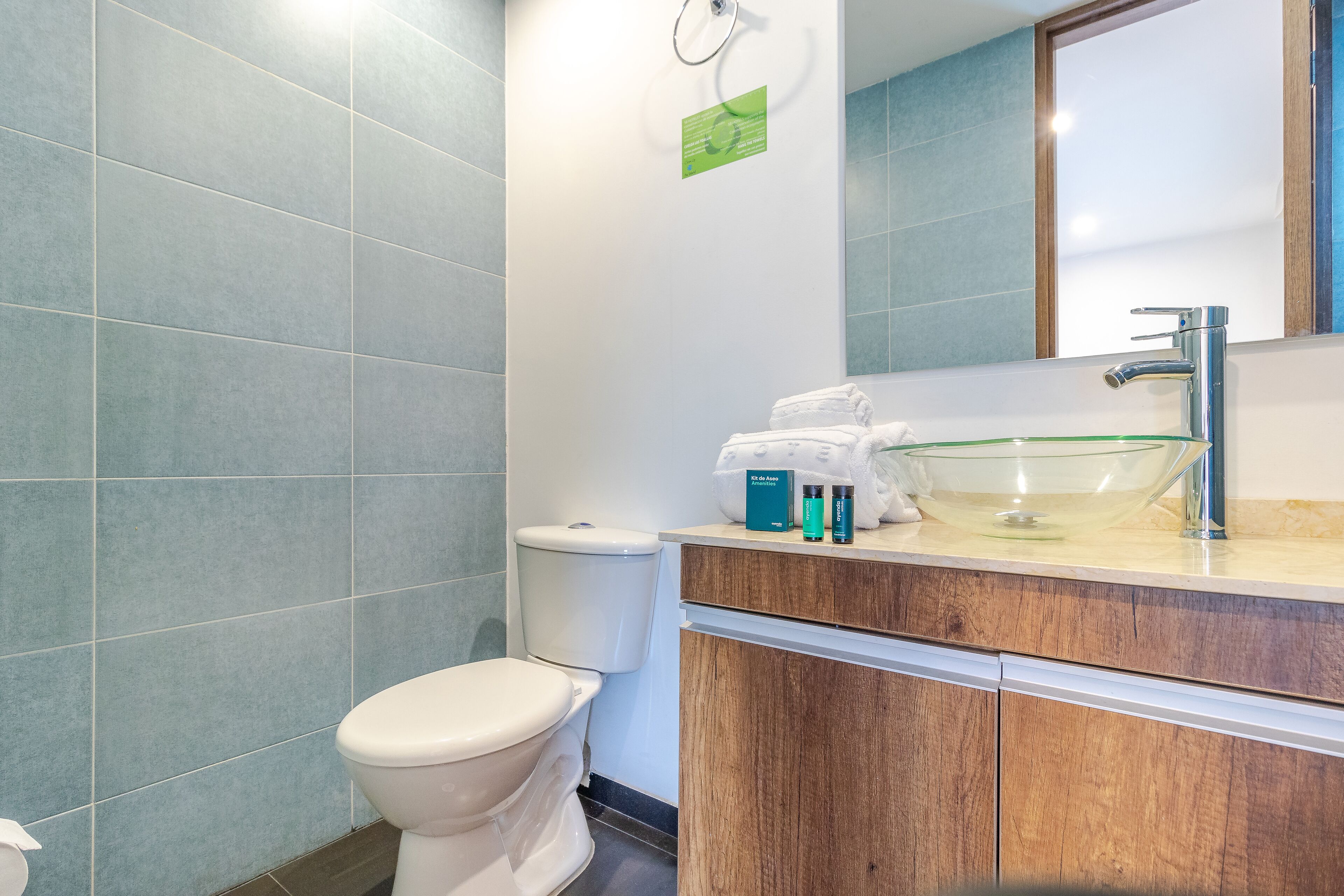 A modern bathroom with a toilet, a glass sink, and a wooden vanity.