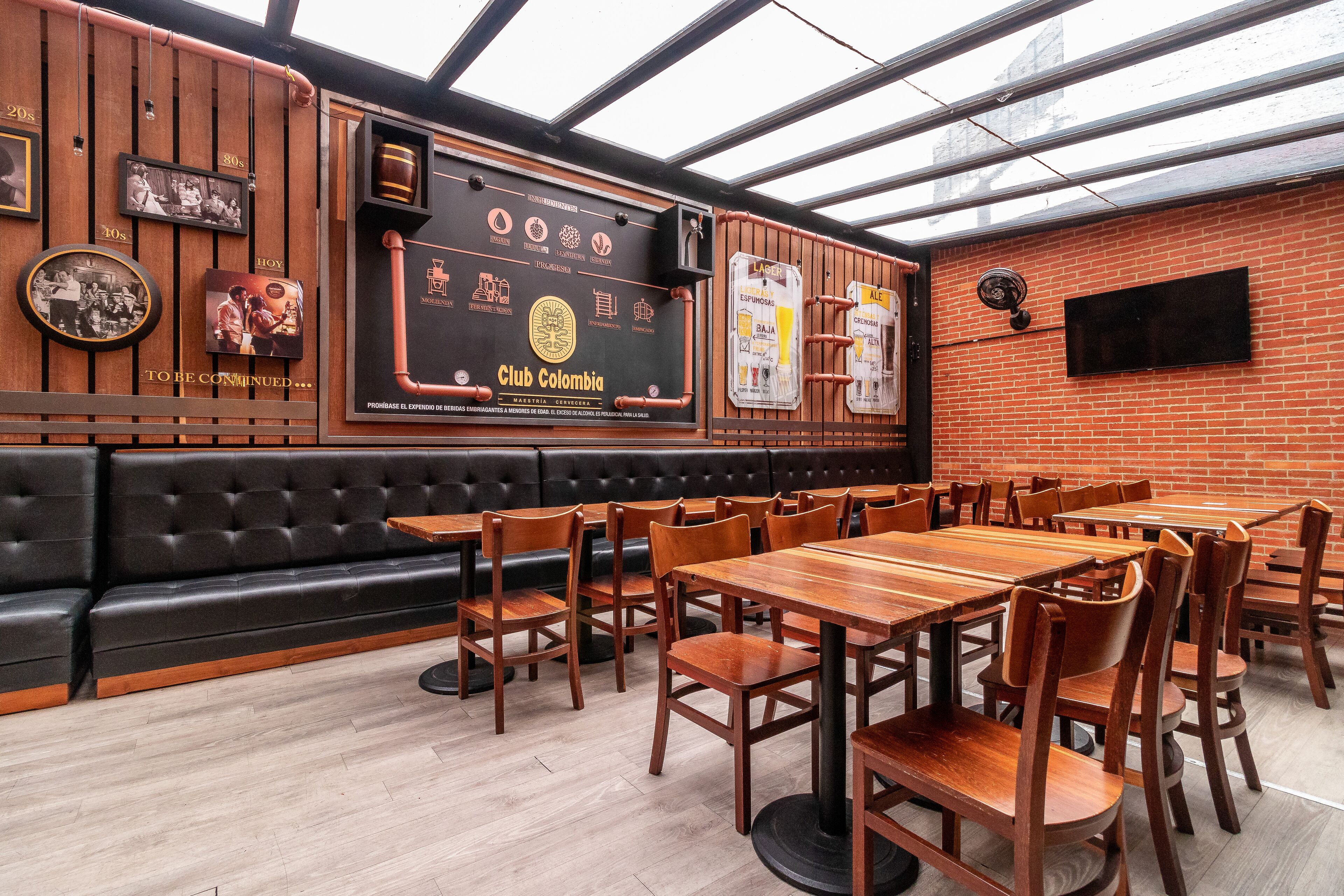 A restaurant interior with wooden tables and chairs, a black leather booth, and a large menu board.