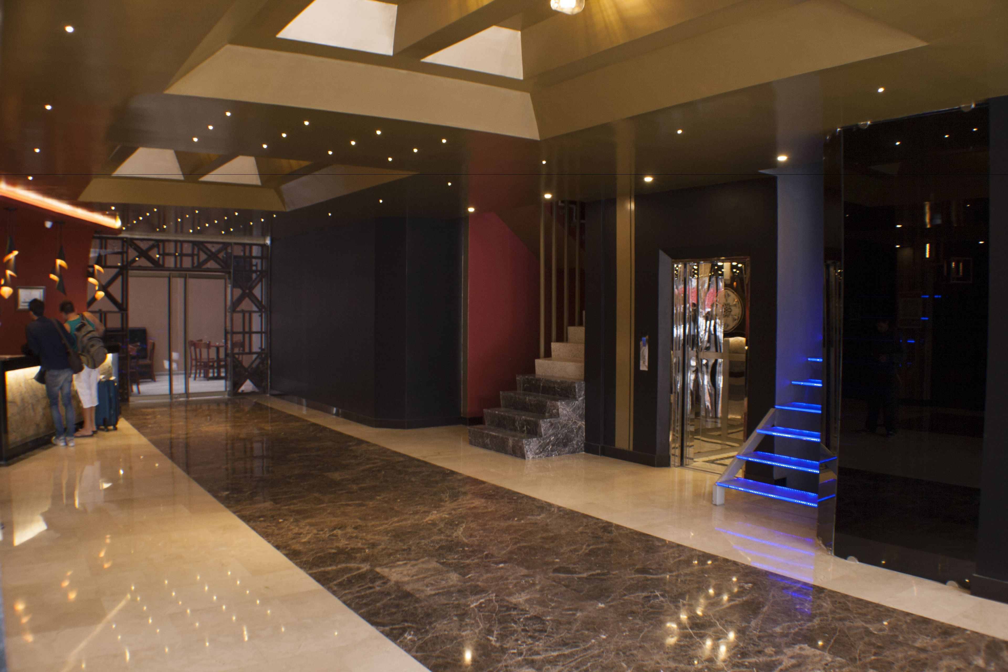 A spacious lobby with a marble floor, a staircase with blue lighting, and a reception desk.