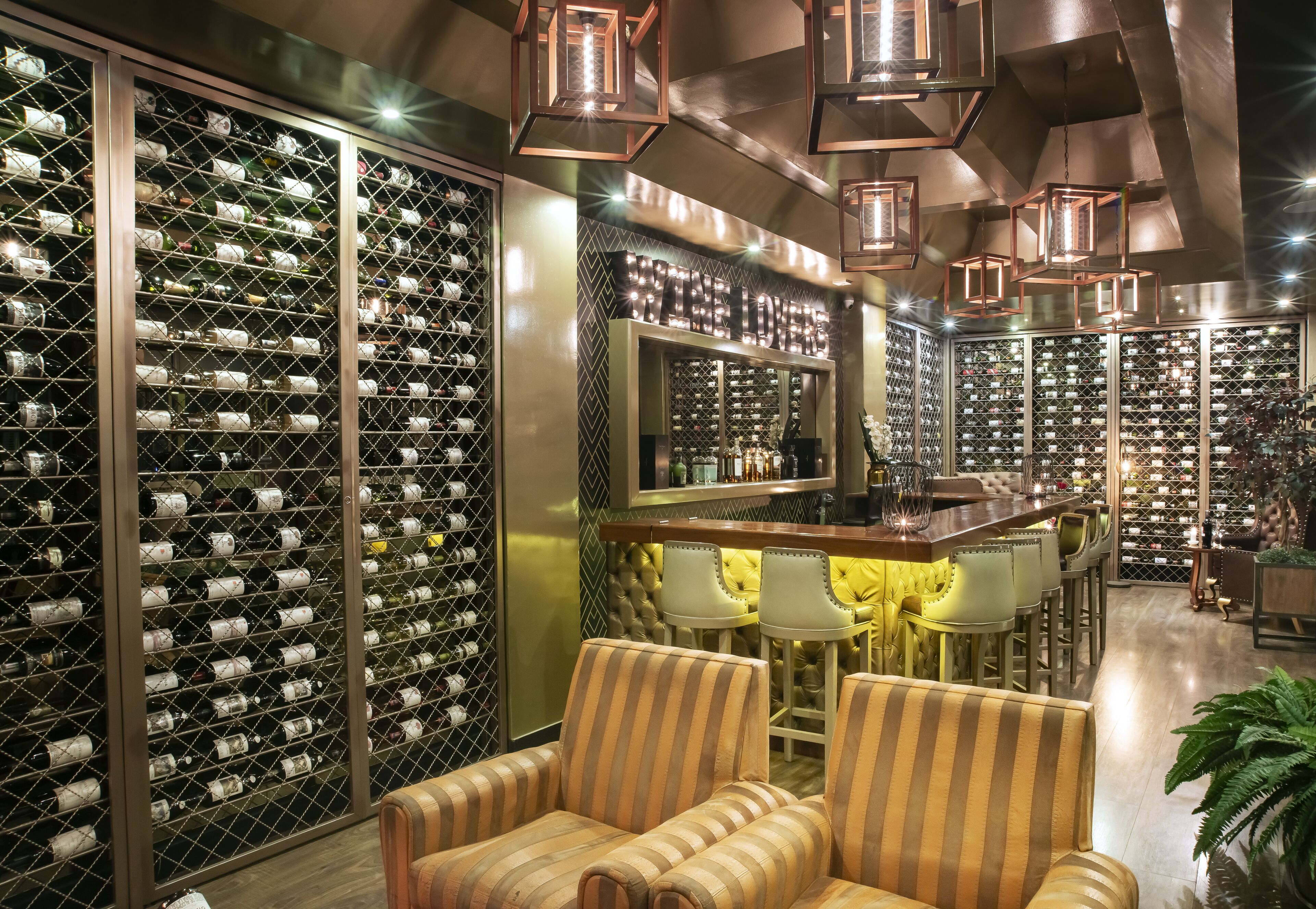Una bodega con hileras de botellas de vino, una zona de bar con taburetes y un área de estar con sillas a rayas.