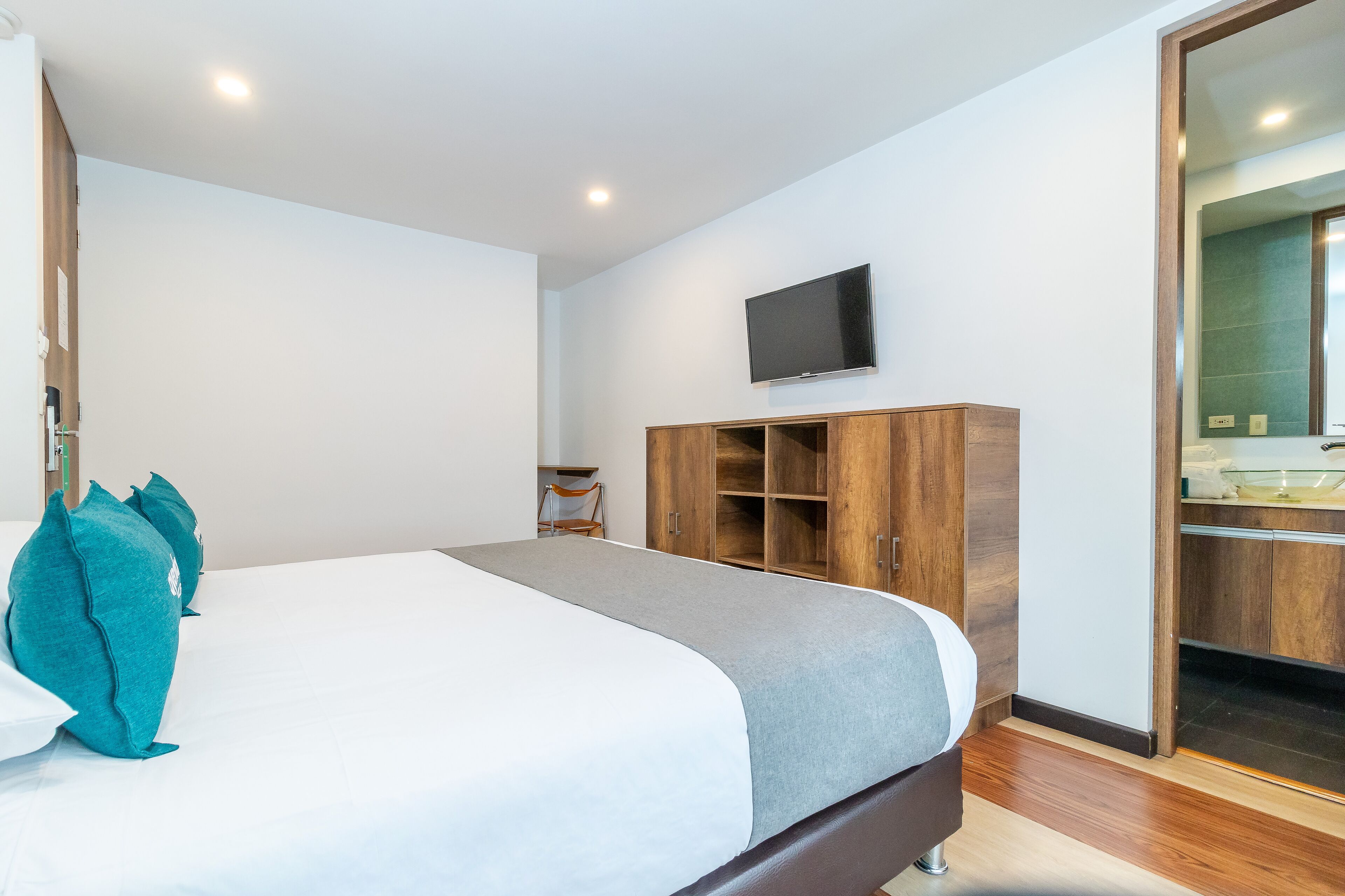 Una habitación de hotel moderna con una cama grande, un televisor montado en la pared y un armario de madera.