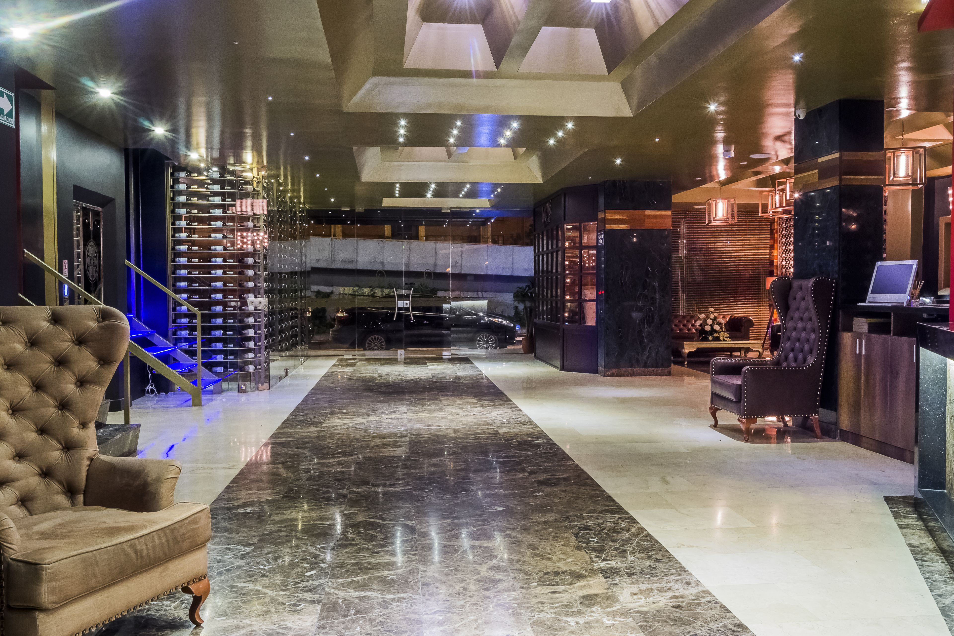 A spacious lobby with a marble floor, a grand staircase, and a seating area with a leather armchair and a sofa.