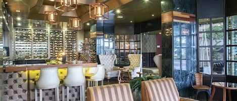 Una zona de bar con estantería para vinos, taburetes acolchados y un espacio de estar con sofás y sillones a rayas.