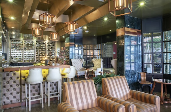 A bar area with a wine rack, cushioned bar stools, and a seating area with striped sofas and chairs.