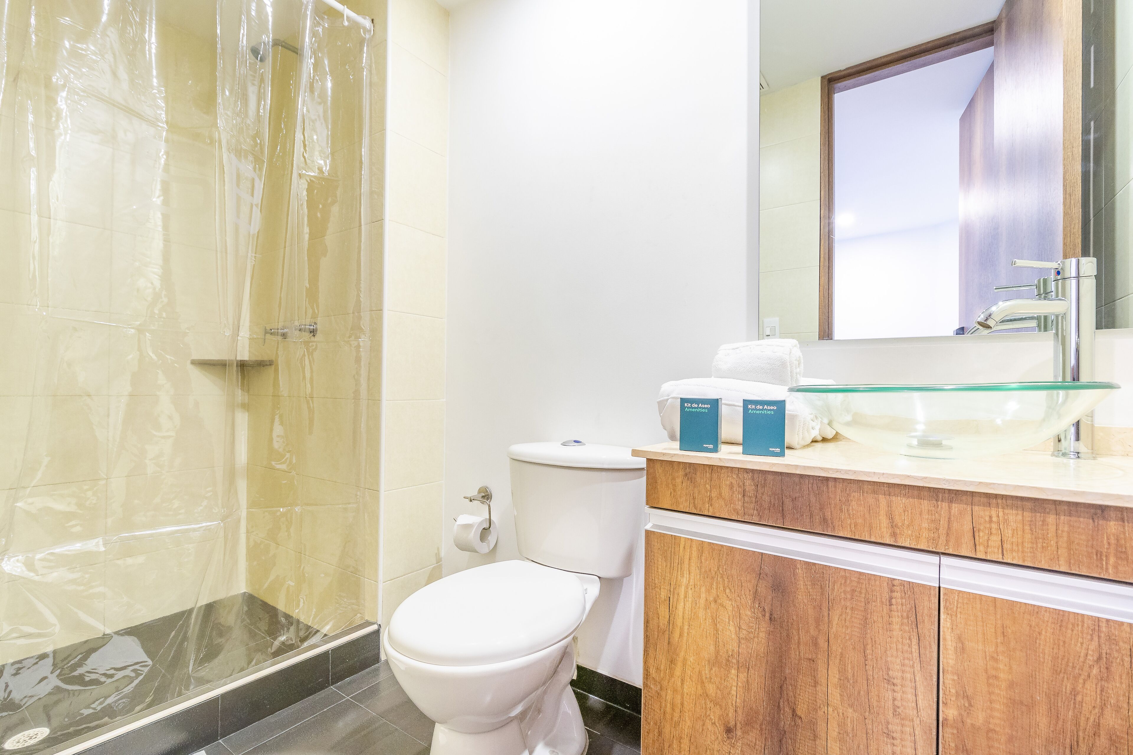 A bathroom with a glass shower enclosure, a white toilet, and a wooden vanity with a glass bowl sink.