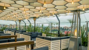 Un salón en la azotea con paneles hexagonales en el techo, zonas de estar y vistas a la ciudad.