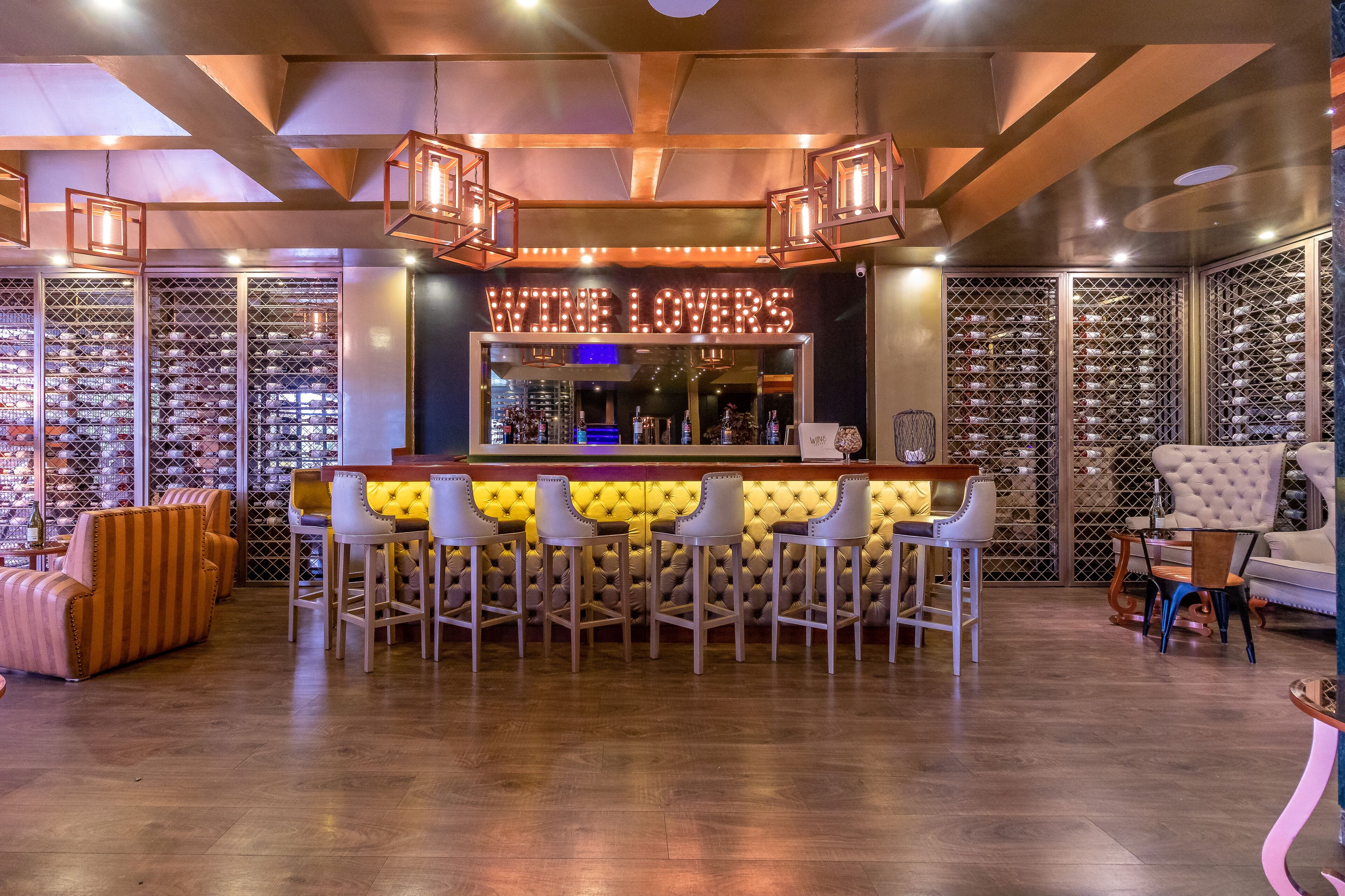 Zona de bar con una vinoteca, taburetes y un espacio de estar con un sofá y sillones.
