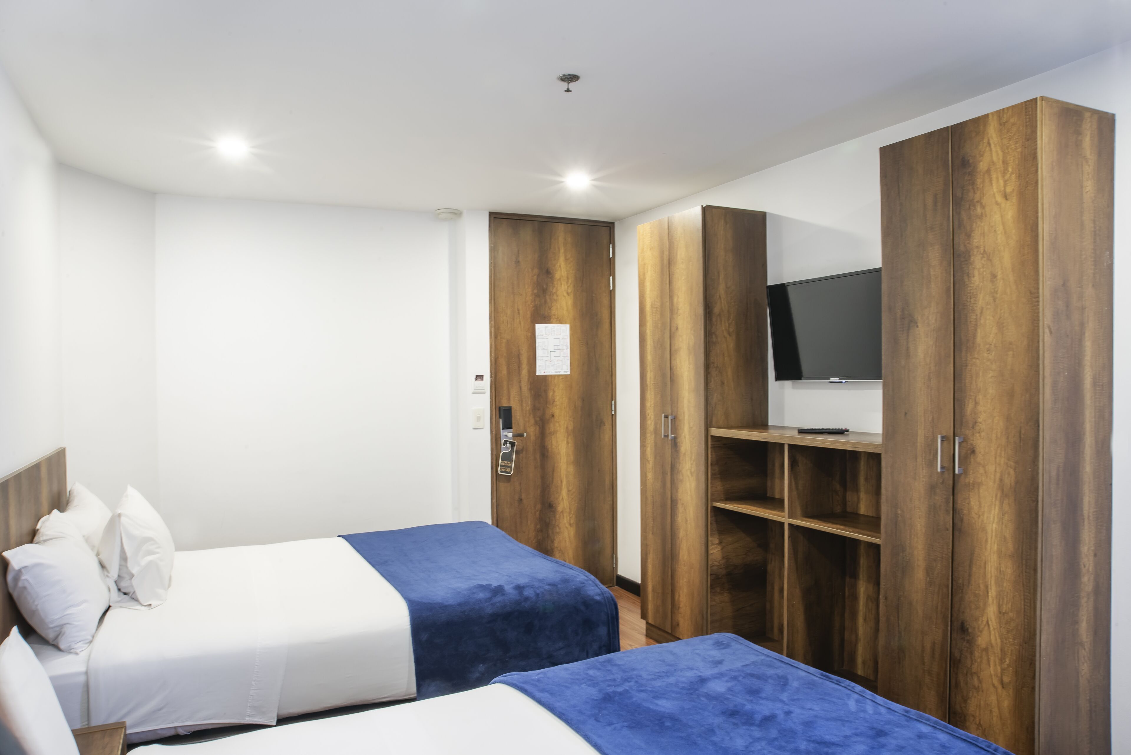 A hotel room with two beds, wooden wardrobes, a television, and a white ceiling.