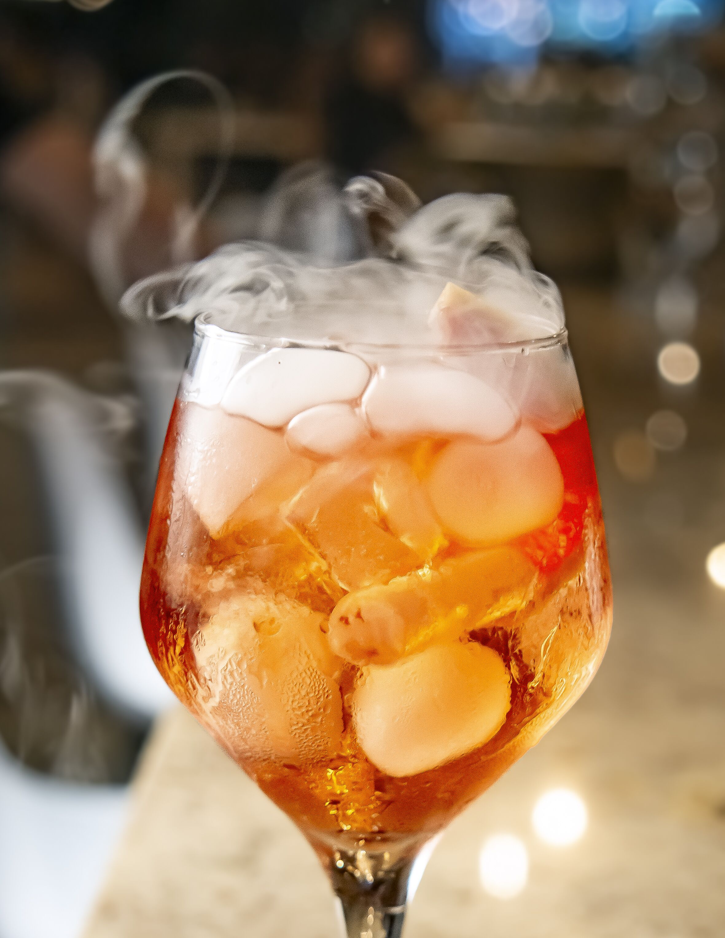 Ein Cocktailglas mit Eiswürfeln und einer klaren Flüssigkeit, vermutlich ein Getränk, aus dem Dampf aufsteigt.