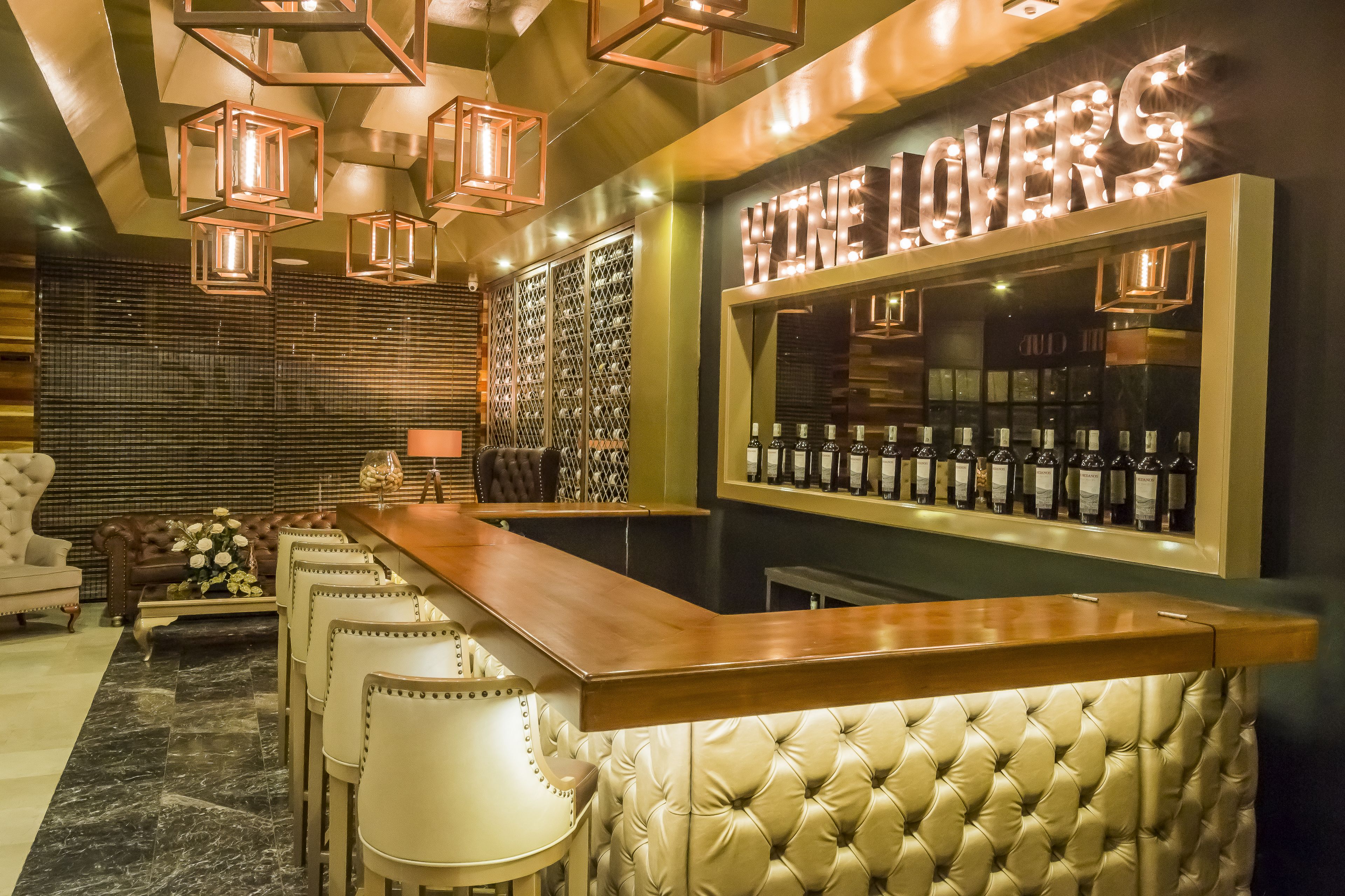A bar area with a wooden counter, bar stools, and a wall of wine bottles.