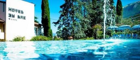 A hotel pool with clear blue water, surrounded by trees and a mountain backdrop.