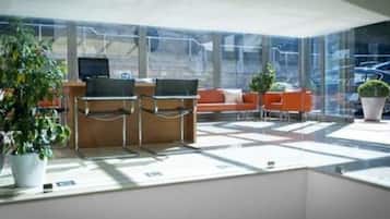 A modern hotel lobby with a glass wall, seating area, and potted plants.