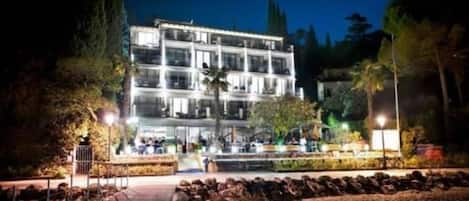 Un hotel de varios pisos con un patio central, rodeado de árboles y una entrada bien iluminada.