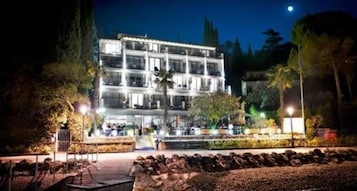 Hotel com vários andares e um pátio central, rodeado por árvores e uma entrada bem iluminada.