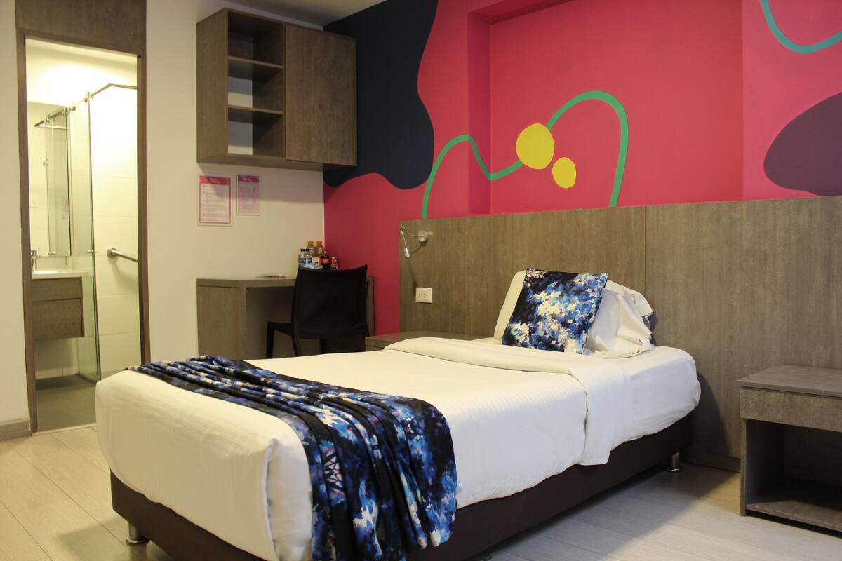 A modern hotel room with a large bed, a desk, and a shower area.