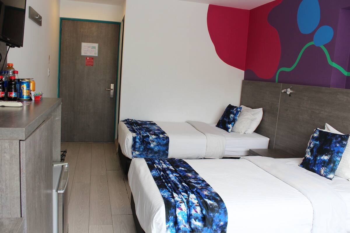 A hotel room with two beds, a desk with a computer, and a wall with a colorful abstract design.