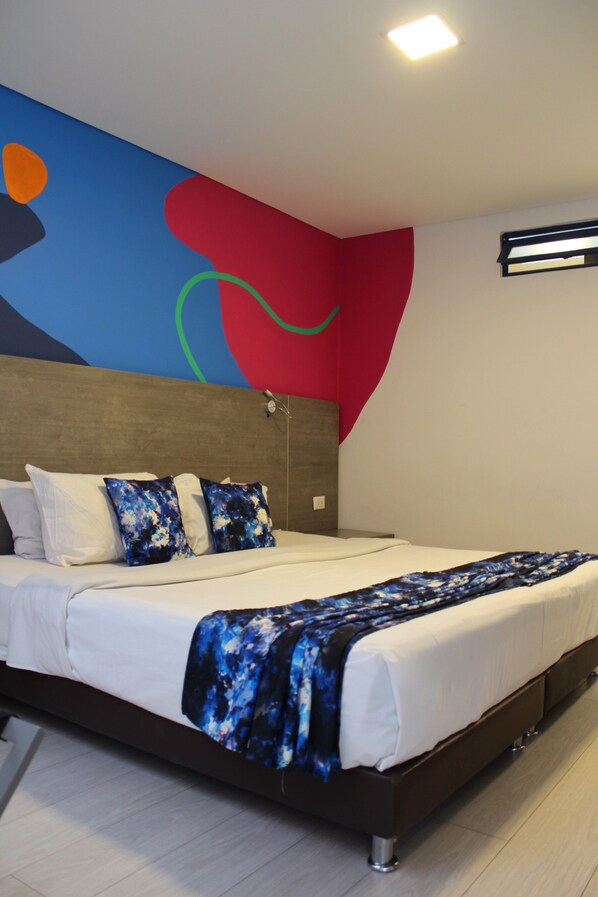 A modern hotel room with a large bed, a headboard with a geometric design, and a colorful abstract mural on the wall.