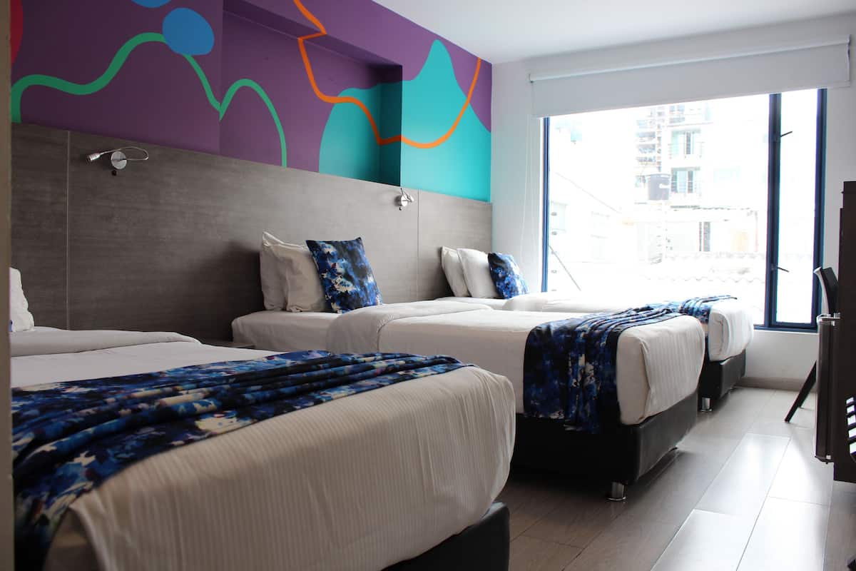 A hotel room with two beds, a large window, and a colorful abstract wall design.