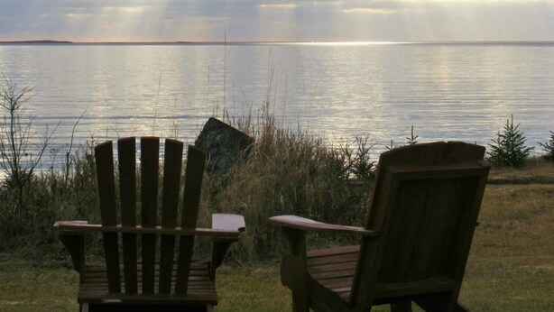 Two wooden Adirondack chairs facing a calm lake with a distant shoreline. - Seawind Landing Country Inn (Charlos Cove)