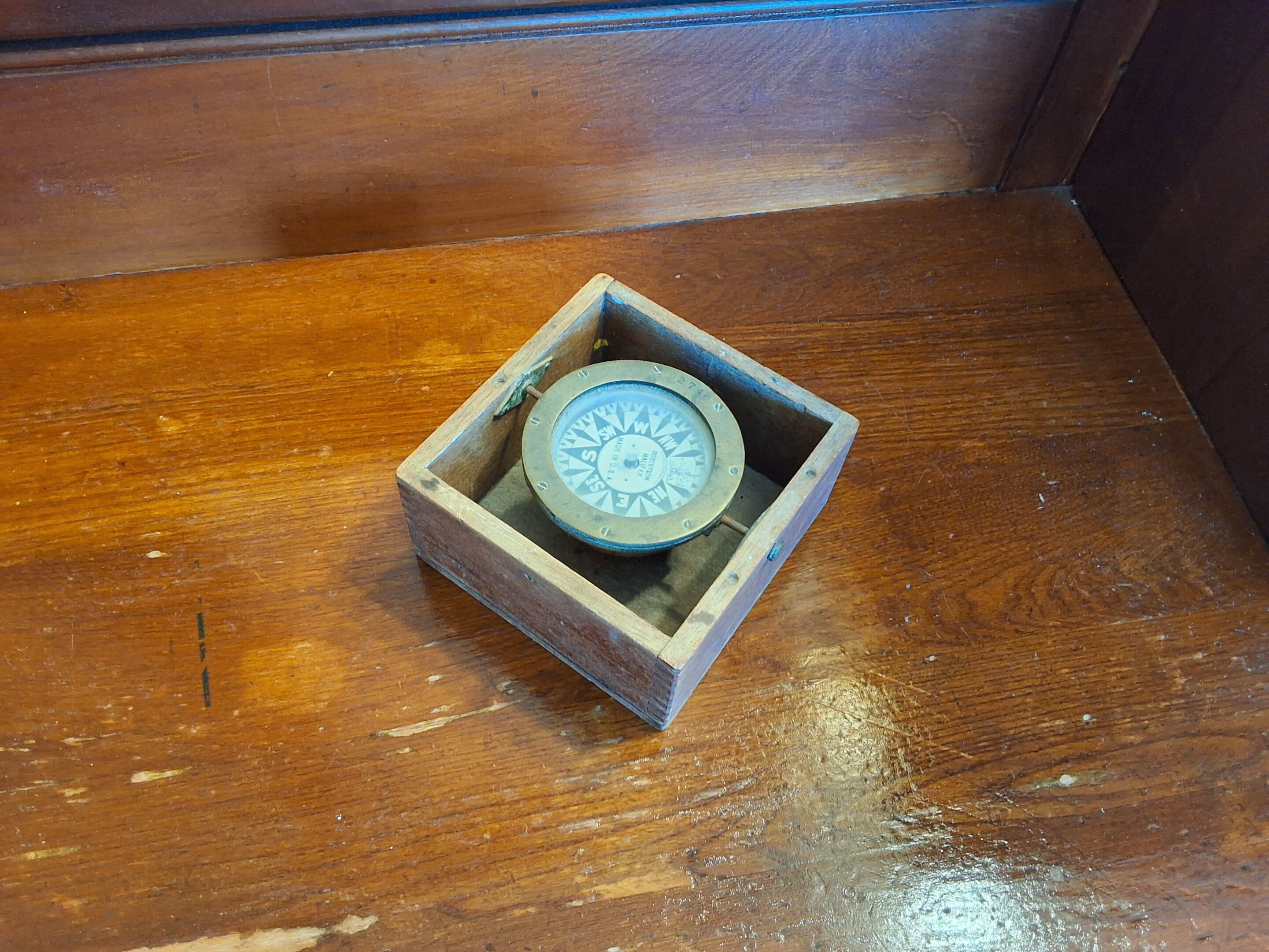 A compass in a wooden box on a wooden floor.