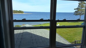 A window with a view of a grassy area, a paved path, and a body of water. - Seawind Landing Country Inn (Charlos Cove)