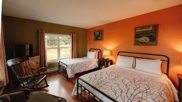 A hotel room with two beds, a wooden rocking chair, a TV, and a window with curtains.
