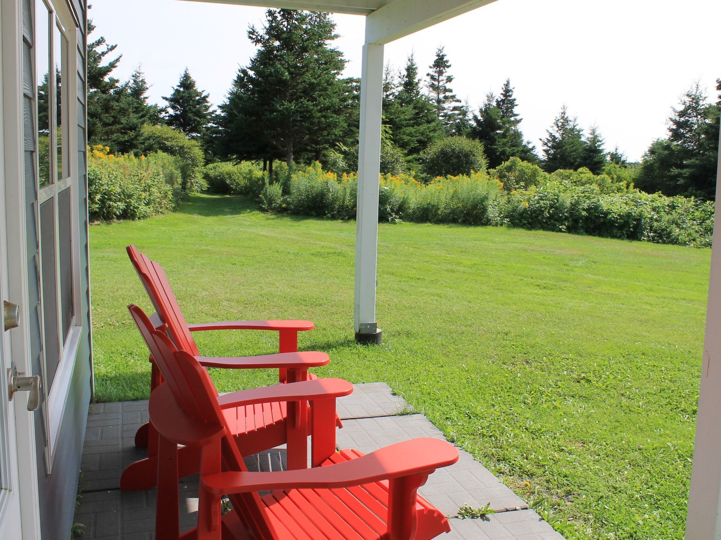 A covered patio with red Adirondack chairs and a white column.