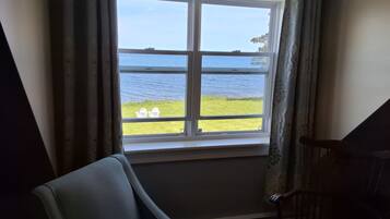 A room with a large window overlooking a body of water and grassy area.