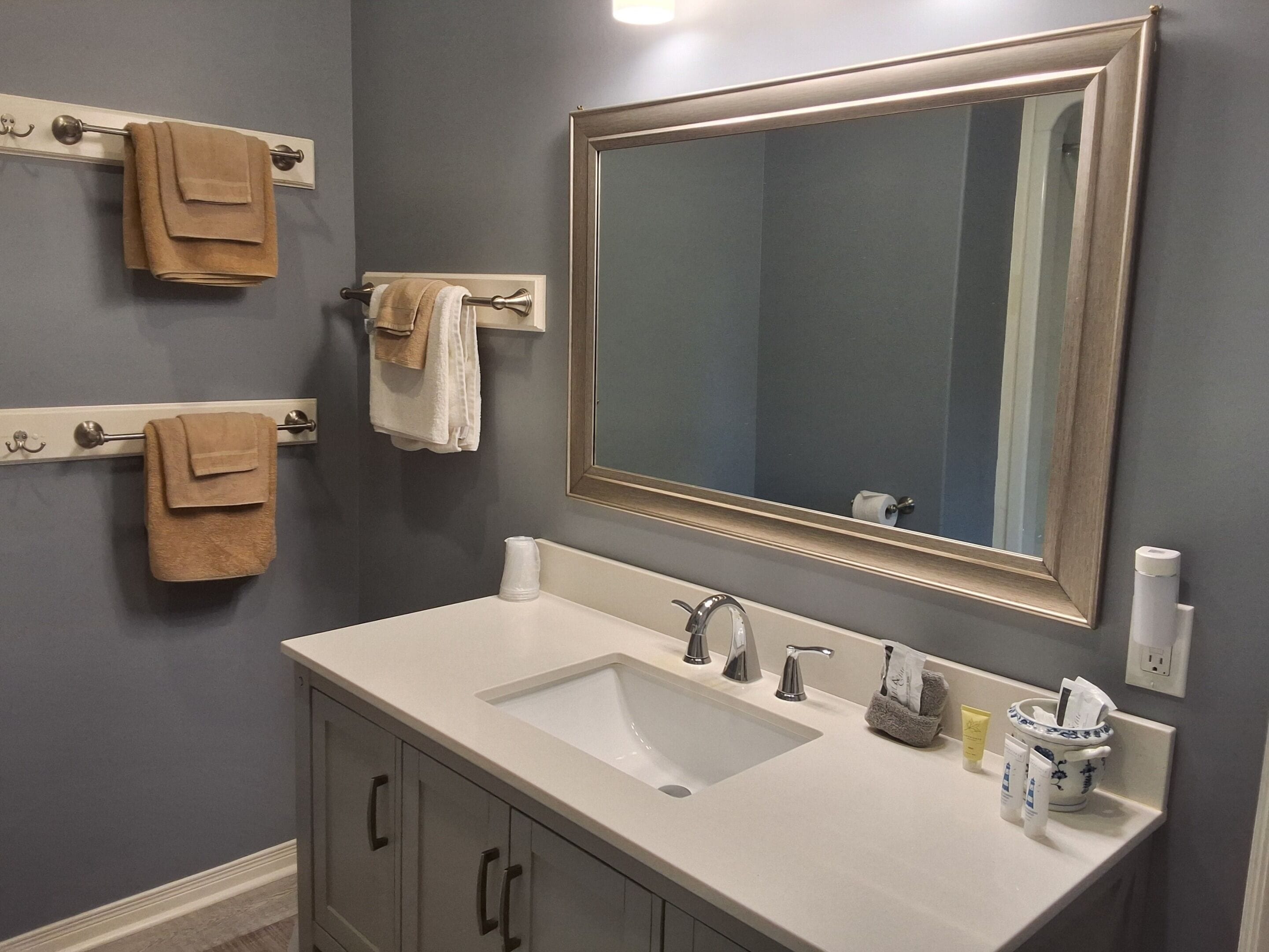 A bathroom with a large mirror, a sink with two faucets, and towel racks with folded towels.
