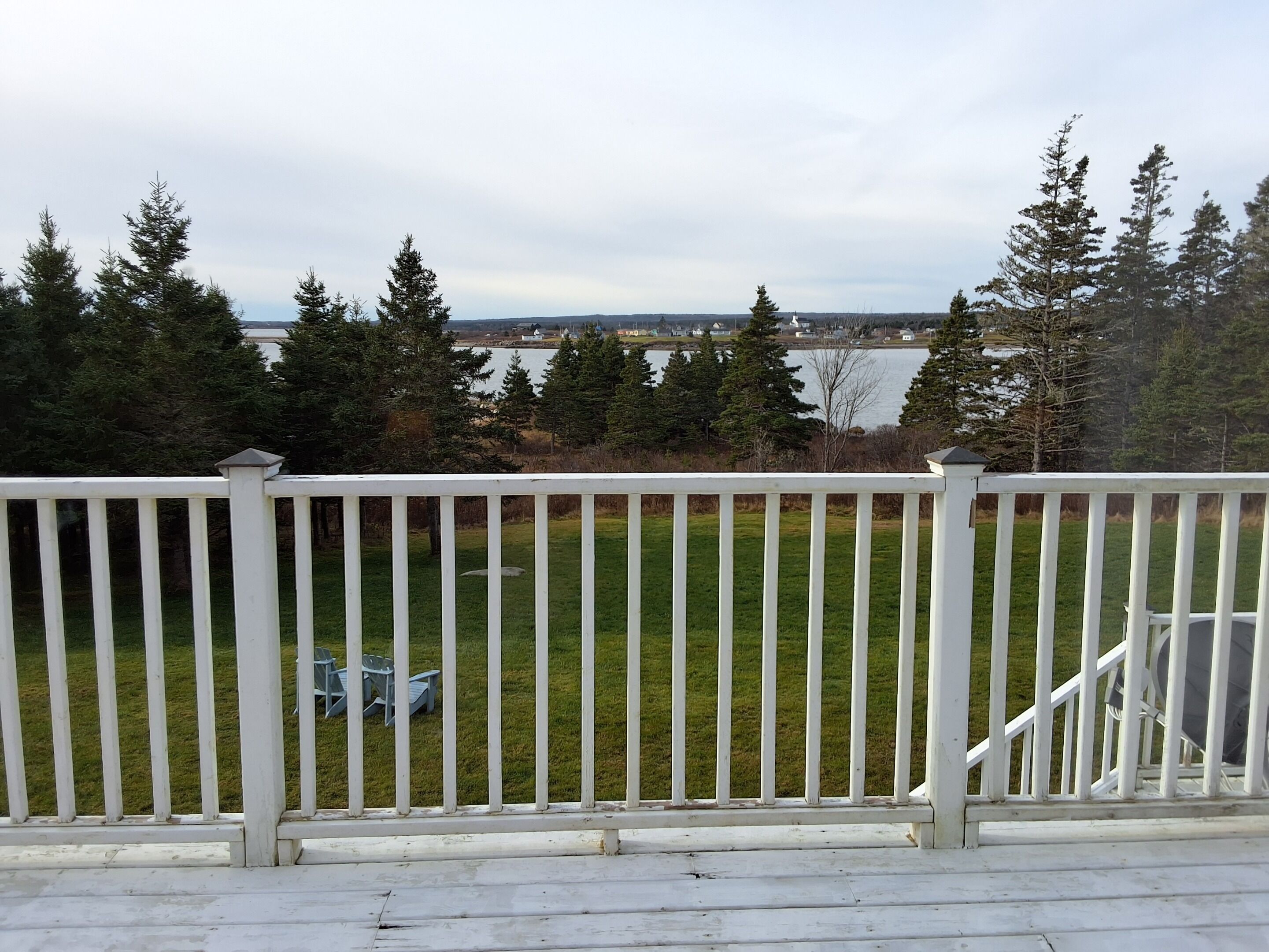 A deck with a white railing overlooking a grassy area with trees and a body of water in the background.