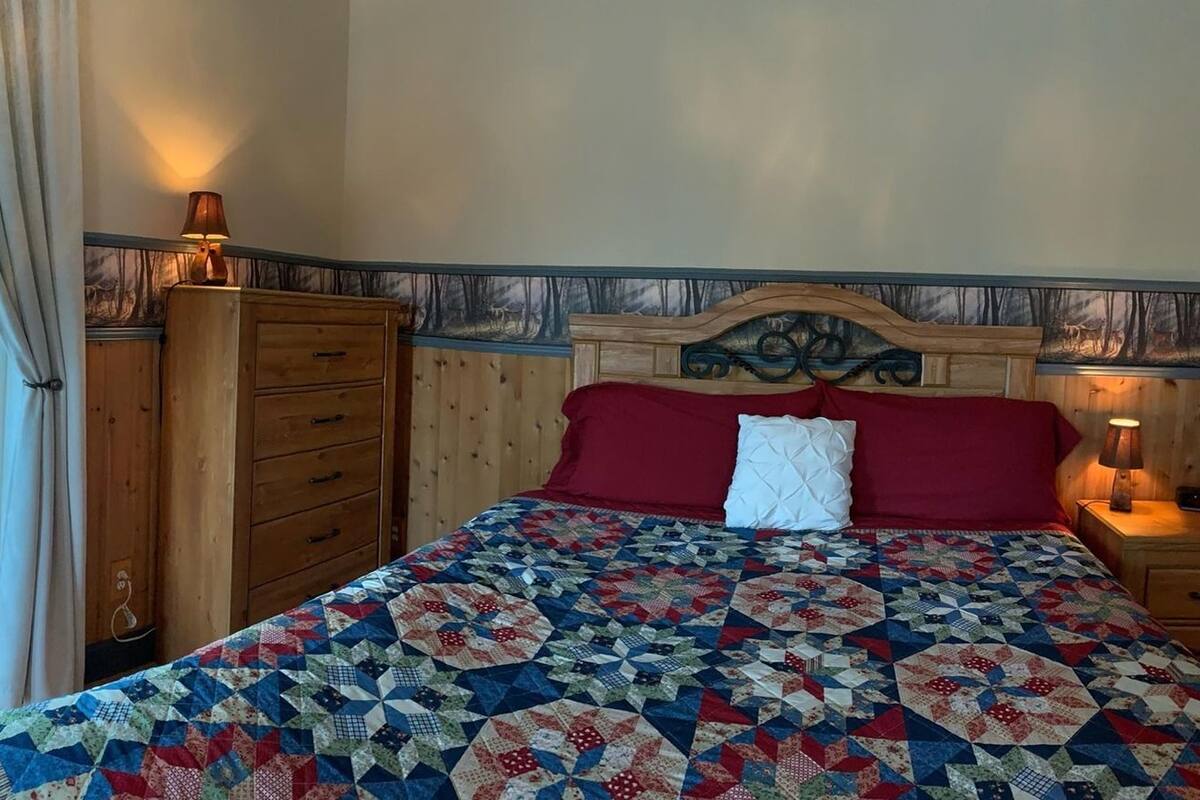 Un dormitorio con chimenea, un ventanal grande, una cama con colcha y un aparador de madera.